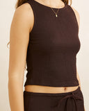A close-up of a model wearing a dark brown ribbed knit sleeveless crop top and matching dark brown drawstring pants against a light beige background. Rhythm Indie High Neck Tank - Chocolate