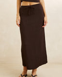 A dark brown ribbed knit midi skirt with a tie waist, shown on a model against a neutral beige background. Front view of the chocolate brown Rhythm Indie Maxi Skirt showing the high-rise waist and clean straight column silhouette.