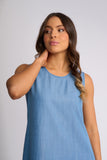 A woman wearing a sleeveless light blue top, shown from the chest up against a plain light gray studio background.