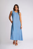 A woman modeling a sleeveless, light blue midi dress with a relaxed, A-line silhouette, paired with brown leather wedge sandals, against a plain light gray studio background.