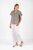 Woman wearing a gray patterned top and white pants on a white background Front view of the Knewe Label Addison Top in Ink Gingham navy and white check, showcasing the elegant neckline and relaxed fit layout.