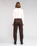 Person wearing a white blouse and brown pants on a plain background