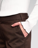 Brown pants with a white shirt and hand in pocket