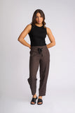 A woman modeling a pair of dark brown wide-leg cropped pants with a black drawstring waist, paired with a black sleeveless top and black slide sandals, against a light gray studio background. Detailed close-up macro view of the premium stretch fabrication texture, rich chocolate brown weave, and high-quality stitching on the Knewe Label pants.