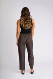 A woman viewed from the back wearing dark brown wide-leg cropped pants, a black sleeveless top, and black flat shoes against a light gray studio background. Back view of the Knewe Label Dew Pant in Chocolate, displaying the smooth, sculpted fit and premium fabric draping.