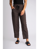 A model wearing dark brown cropped pants with a black drawstring waist, paired with a black top and black slide sandals, photographed against a light gray studio background. Front view of the Knewe Label Dew Pant in Chocolate brown, showcasing the clean tailored front and flattering waistband layout.