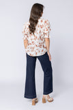 Woman wearing a floral blouse and dark jeans on a white background