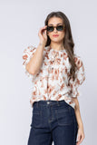 Woman wearing a floral blouse and sunglasses against a plain background