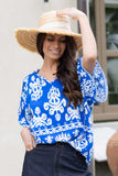 Woman wearing a blue and white patterned blouse with a straw hat outdoors.