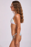 A woman in side profile wearing a light blue and white patterned string bikini with a tie detail on the left side, set against a plain light gray studio background.