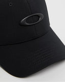 Oakley Tincan Cap in Black and Carbon Fibre close up view highlighting the textured metal ellipse front icon and moisture wicking internal sweatband, sold by Point Break Cambridge local family surf shop at 63 Duke street.