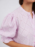 Close-up of a person wearing a pink blouse with intricate detailing on a plain background