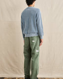 A person shown from the back wearing a light blue knit sweater and olive green cargo pants with visible Levi's patches, standing against a beige fabric backdrop. Rhythm Mens Polu Crew Knit - Washed Blue