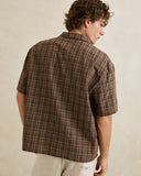 A man wearing a brown short-sleeve plaid button-down shirt, shown from the back against a neutral beige background. Rhythm Mens Relaxed Brady Check SS Shirt - Coffee
