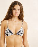 Woman wearing a black and white patterned bikini against a beige background. Close up detail of the premium cream floral stretch fabric, clean stitch detailing, and adjustable string channels on the Rhythm bikini top.