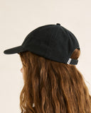 A person shown in side profile wearing a black baseball cap with long wavy brown hair against a plain light beige background. Rhythm Essentials Cap - Black