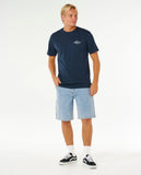 Man wearing a navy t-shirt and light blue shorts on a white background