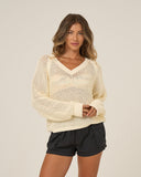 Woman wearing a beige knitted sweater and black shorts on a plain background. Front view of the Salty Crew Women's Surge Sweater in Off White, showing the V-neckline and premium crochet open-knit pullover design.