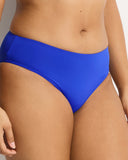 A close-up of a model wearing a bright royal blue bikini bottom against a light gray studio background. Detailed close-up macro view of the premium recycled eco fabric texture and high-quality stitching on the Cobalt Sea Level swim pants.