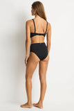 Woman wearing a black bikini on a white background Back view of the Sea Level Essentials Retro High Waist Bikini Pant in Black, displaying the elegant full rear coverage and high-quality fabric finish.