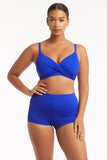 A woman modeling a bright royal blue two-piece swimsuit consisting of a ruched crossover bikini top and matching high-waisted shorts, set against a plain white studio background.