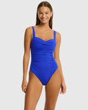 A woman modeling a bright royal blue one-piece swimsuit with a ruched sweetheart bodice and shoulder straps, photographed against a light gray studio background. Front view of the Sea Level Essentials Twist Front Multifit One Piece Swimsuit in Cobalt blue, showing the crossover twist neckline.