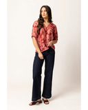 Front view of the Seeking Lola Essence Top in Pink Bloom floral print, showcasing the elegant neckline and relaxed fit layout. A woman modeling a short-sleeve button-up blouse with a dusty rose and red abstract floral pattern, paired with dark wide-leg jeans and brown heeled sandals, against a plain off-white studio background.