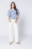 Woman wearing a blue patterned top and white pants on a white background