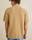 A man viewed from the back wearing a short-sleeve waffle-knit camp collar shirt in a warm tan color, paired with blue jeans against a neutral beige background. Rhythm Mens Textured Knit SS Shirt - Sand