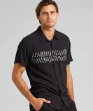 Front view of The Mad Hueys Port Side Ahoy Fkrs Woven Short Sleeve Shirt in Black showing the relaxed fit, camp collar, and custom graphic print. A man wearing a black collared shirt with a sublimated print across the chest. The shirt has a button-up front and a left chest pocket.
