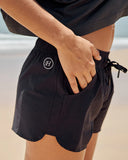 Person wearing black shorts with a mad hueys logo on a beach