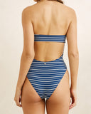 Rear view of a woman wearing a blue and white striped high-waisted bikini bottom with a matching bandeau-style top, set against a plain beige background.