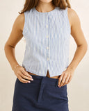A woman wearing a sleeveless button-front top with vertical light blue and white stripes, paired with navy pants, against a plain beige background. Rhythm Vista Stripe Vest Blue