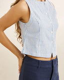A close-up of a woman wearing a sleeveless, cropped top with vertical light blue and white stripes, paired with navy blue pants, against a plain beige background. Rhythm Vista Stripe Vest Blue