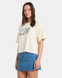 Woman wearing a cream t-shirt with a graphic design and a denim skirt on a white background
