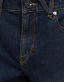 Close-up of dark blue denim jeans showing the waistband, button closure, belt loop, front pocket, and contrast stitching. Close up detail of the premium new vintage blue denim wash, metal pocket rivets, and Volcom branded hardware.