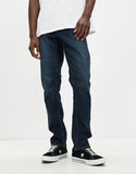 A person wearing dark blue slim-fit denim jeans, a white t-shirt, and black low-top sneakers with white star details, shown from the waist down against a plain white studio background.