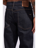 Close-up back view of a person wearing dark indigo denim jeans, showing the waistband, leather patch, back pockets, and a small Volcom logo on the pocket.