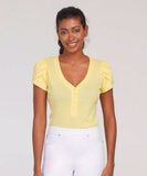 A woman wearing a buttercup yellow short-sleeved henley top with tulip sleeves, paired with white pants.